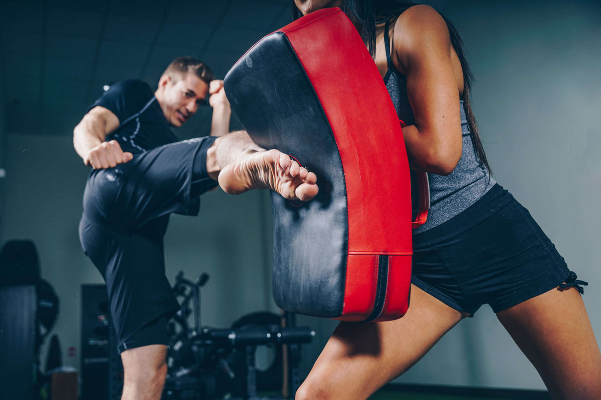 Dos personas entrenando con un escudo de golpes en un gimnasio