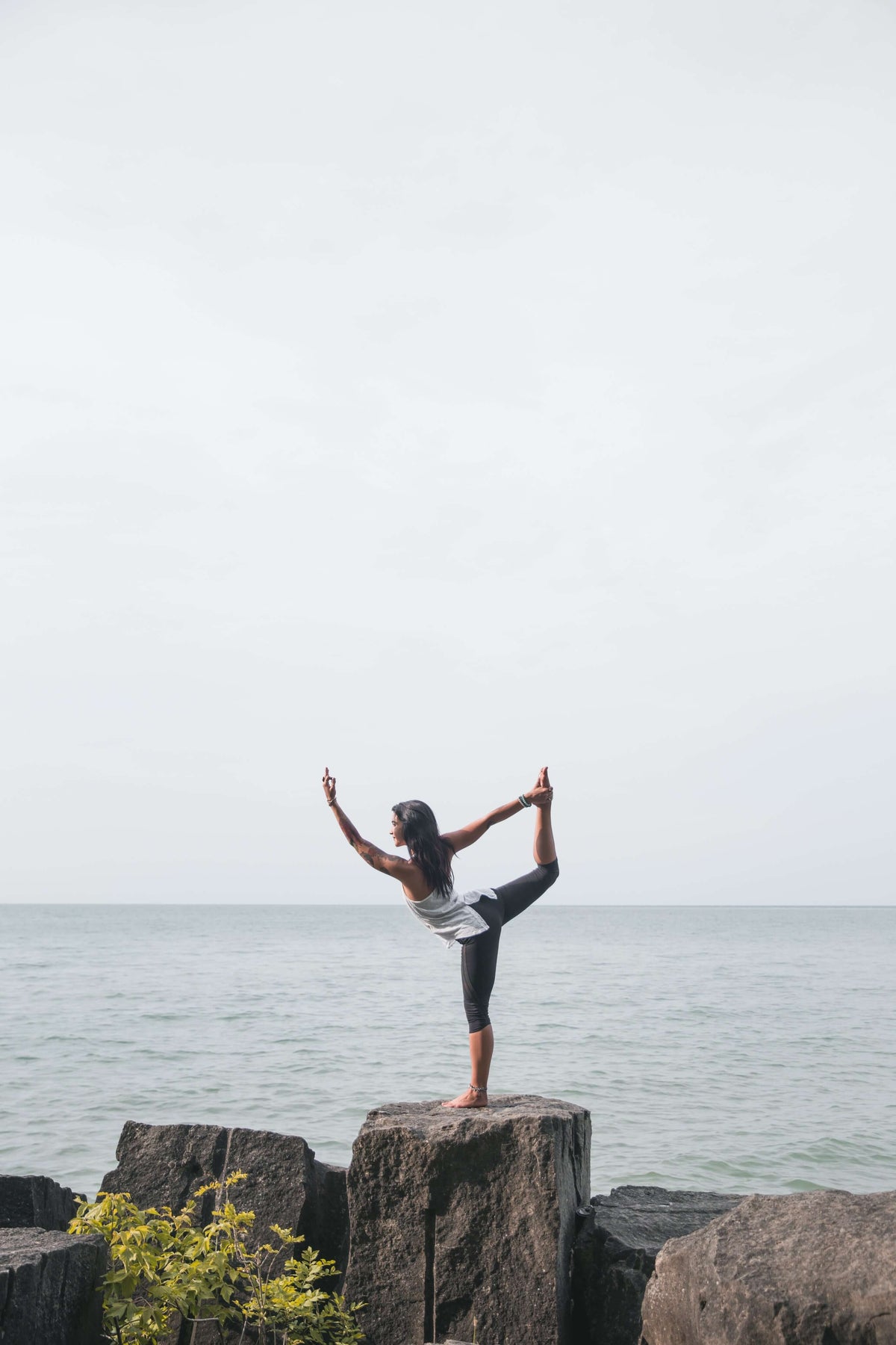 Mujer en postura de yoga sobre rocas frente al mar